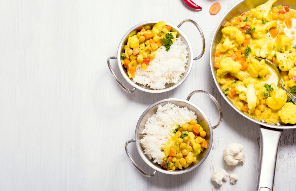 Vegetarian curry with cauliflower and chickpeas served in metal bowls with rice, healthy homemade vegan food, indian cuisine, clean eating concept, copy space background for text