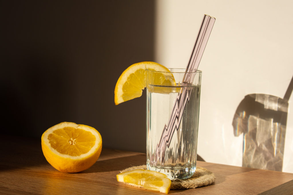 Glass of water with fresh lemon juice with Reusable glass Straws Detox cold tonic water with sunny lemon slices Low-waste lifestyle Eco-Friendly Drinking Straw Set with cleaning brush. Zero waste, plastic free concept